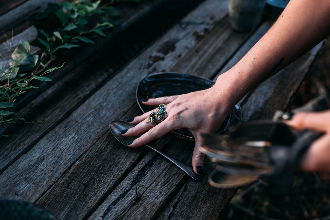 From above of crop anonymous female in rings putting spoon on wooden table against plants in daylight